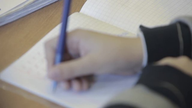 Teenager or kid writing notes with a pen in notebook lying at the desk. Kids in primary school. Handheld close up shot. 