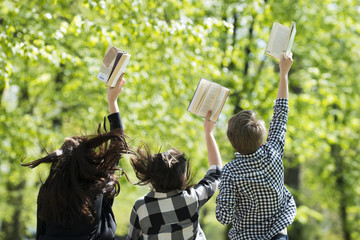 Młodzi ludzie skaczą z książkami w parku wiosną na świeżym powietrzu - obrazy, fototapety, plakaty