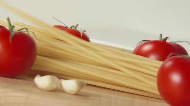 SLOW: A spaghetti fall on a table between a ripe tomatoes and garlic