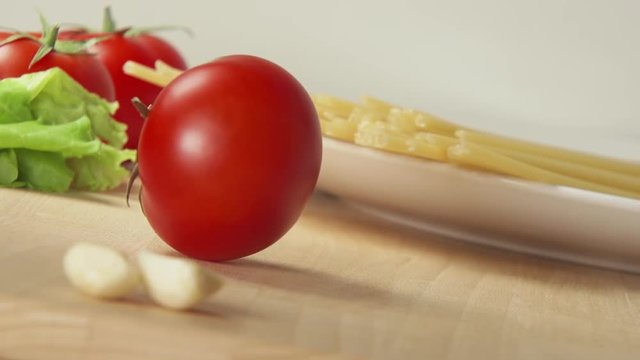 SLOW MOTION: A ripe tomato rolls on a table near spaghetti and garlic