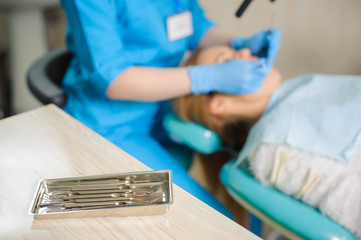 Dentistry tools on foreground and dentist working on woman patient's teeth on the background. Medical equipment. Oral procedure concept.