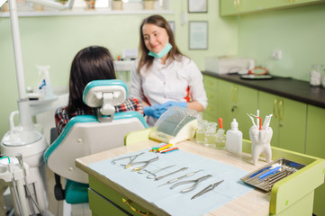 Obraz premium Dental instruments and tools on the foreground and female doctor dentist with patient on the background in a dentist's clinic.