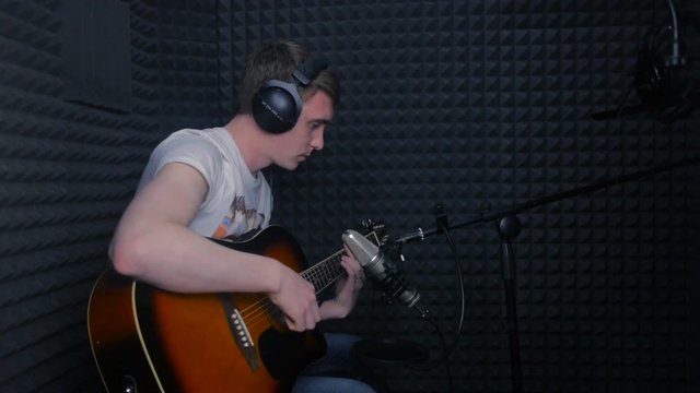 Man playing guitar, recording a song in professional sound studio. HD.