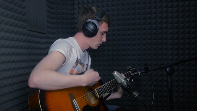 Man playing guitar, recording a song in professional sound studio. HD.