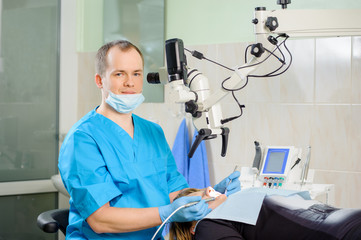 Naklejka na ściany i meble Male dentist working with microscope at modern dentist clinic. Teeth care and tooth health. Dentist checking patient teeth. Oral procedure concept. Stomatology equipment