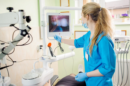 Woman dentist looking at the live picture of teeth on computer in modern dental office. Dental care and treatment. Back view.