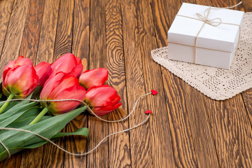 Red tulip bouquet and a gift box on a wooden table.