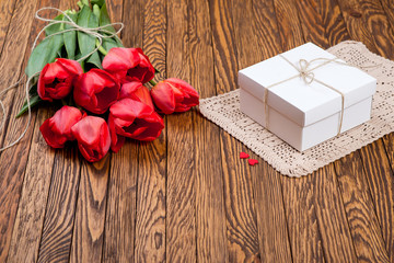 Red tulip bouquet and a gift box on a wooden table.