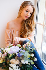 Young blonde woman with a bouquet of flowers sitting near window. Tender portrait in a morning