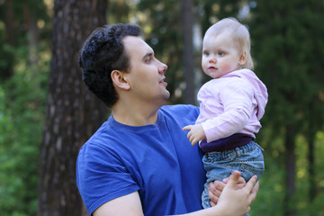 Young handsome man holds his little cute daughter in summer park