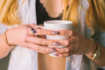 Young woman in underwear holding cup of coffee next to window in the morning, body detail 