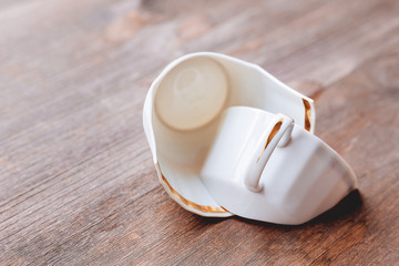 Broken white cup on wooden background. Damaged mug with golden decoration.