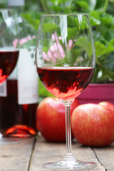Single wine glass on a wooden table with apples in the background.