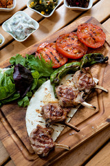 Delicious grilled marinated lamb chops and roasted vegetables from a summer BBQ on a wooden chopping board in a country kitchen