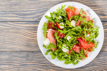 Arugula, prosciutto, mozzarella salad on a white dish