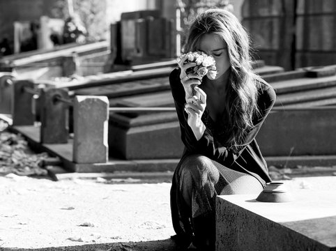 Sad woman holding bunch of flowers near a grave monochrome
