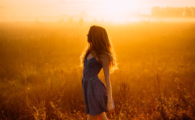 Side view of beautiful girl in fog, field, sun backlight, sunrise, orange colors