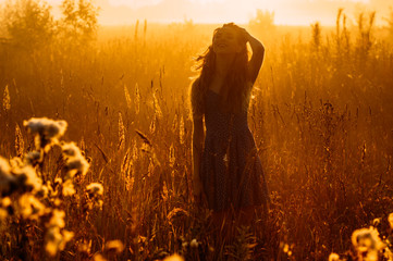Smiling beautiful girl in fog correct her hair, field, sun backlight, sunrise, orange colors