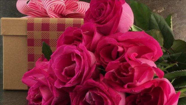 Placing pink roses with beautifully wrapped gift against a slate background for Mothers Day or Valentine gift, slow motion static. 