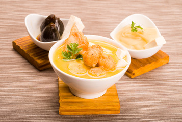 Traditional fanesca serving sitting on wooden surface with accessories next to it such as molo mashed potatoes and fig dessert