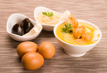 Traditional fanesca serving sitting on grey textile surface with accessories next to it such as molo mashed potatoes and fig dessert