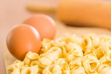 Closeup tortellinis piled up next to an egg and blurry rolling pin background