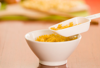 Large kitchen spoon grabbing dry fusilli out from white bowl, professional setting, blurry background