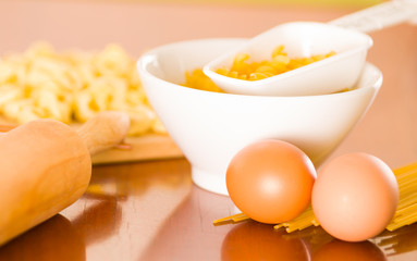 Rolling pin, eggs, pasta and dough spread out on wooden surface