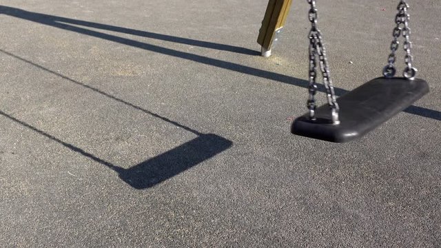 Sunny day with empty swing swaying in wind at playground.
