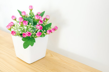 the artificial pink flower in the pot at the wooden table with t