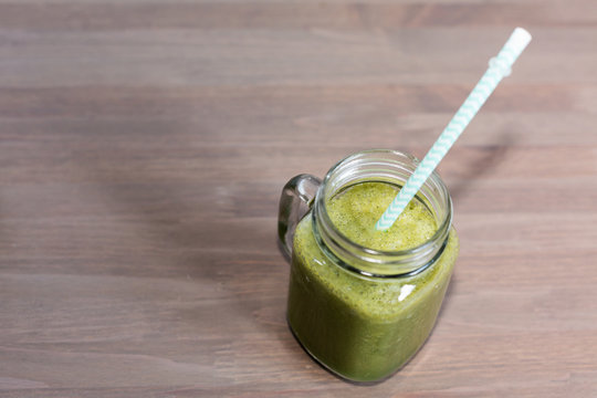Green smoothie in a mason jar with tube on wooden background
