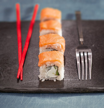 Chopsticks and fork with sushi on black plate