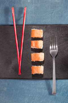 Chopsticks and fork with sushi on black plate