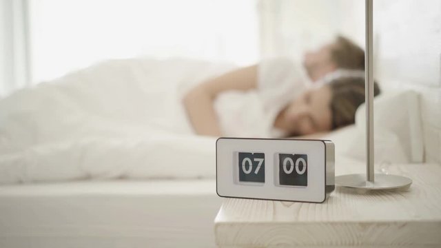 4k footage, alarm clock ringing in the morning, young couple sleeping in their bed don´t want to stand up, focus on clock
