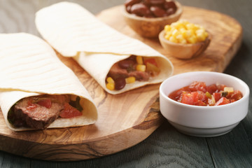 burritos with beef steak, corn, black beans and salsa sauce on wood table, vintage toned