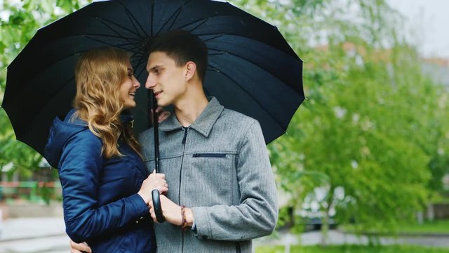 Young woman and a stylish man standing on the street under an umbrella. It's raining