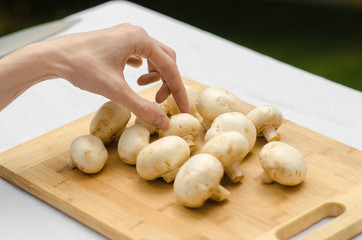 Mushrooms and Food theme: man preparing porcini mushrooms on a wooden board on a background of green grass in summer