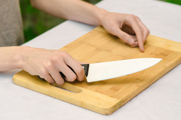 Fototapeta na wymiar cooking theme: a man holding a knife next to a wooden cutting board on a background of green grass in summer