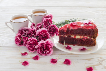 Red velvet cake, two cups of tea and pink carnations on wooden table