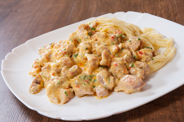 Sliced fried chicken meat in a creamy sauce with spaghetti pasta in a plate on wooden table