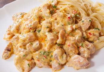 Sliced fried chicken meat in a creamy sauce with spaghetti pasta in a plate on wooden table