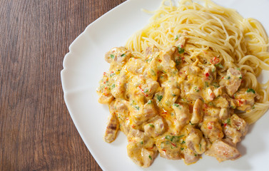 Sliced fried chicken meat in a creamy sauce with spaghetti pasta in a plate on wooden table