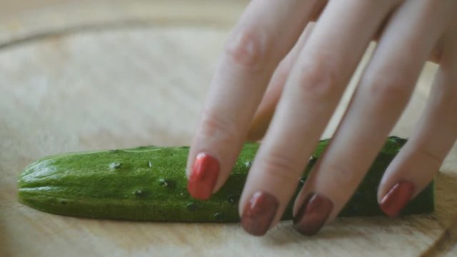 Girl's hands with red nails cut cucumber into slices