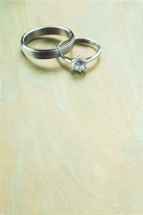 Vertical image of white gold wedding rings on soft pastel background with texture. Wedding invitation background.