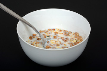 Muesli with a mix of healthy fruit, nuts and seeds and milk in a dish against a black background.