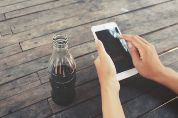 Woman using smart phone with cola drink bottle