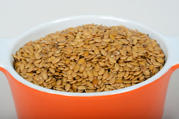 Raw golden linseeds in an orange ramekin dish.