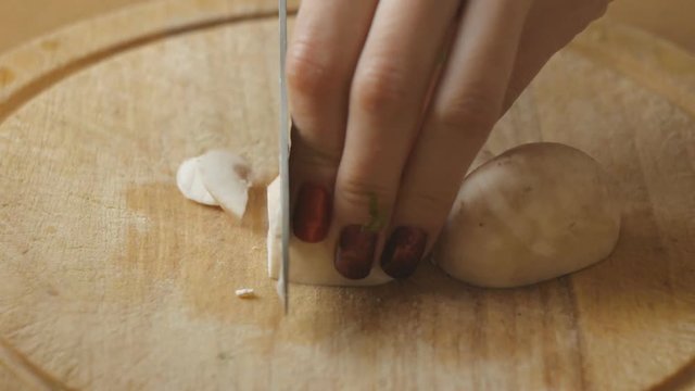Girl's hands with red nails cut champignon into slices