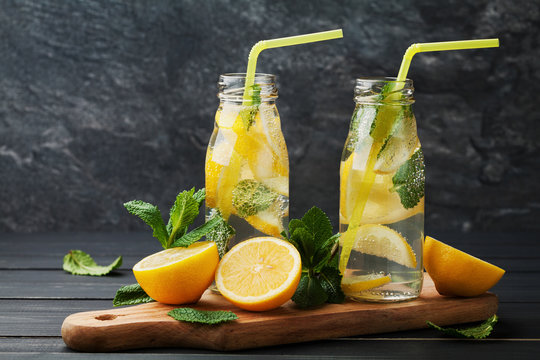 Lemonade drink of soda water, lemon and mint leaves in jar on black background