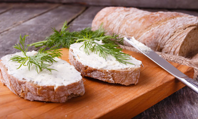 A slice of freshly baked ciabatta bread and healthy low fat cream cheese with dill and fresh green dill on wooden board.